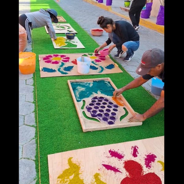 People creating colorful sand art designs on wooden boards laid out on green turf.