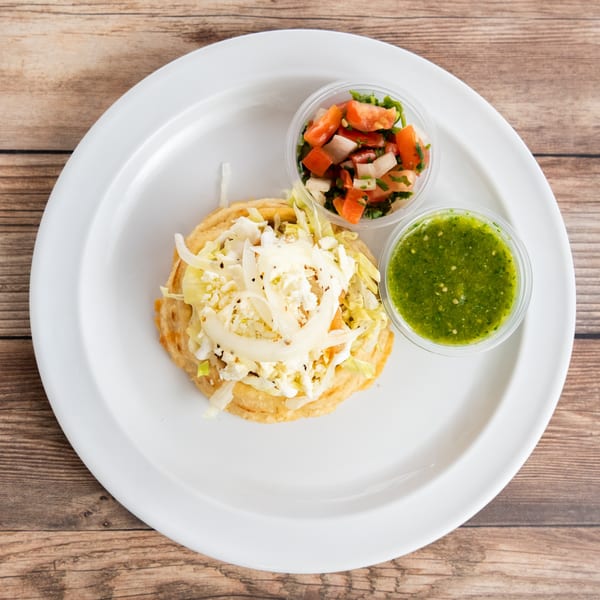 A sope topped with shredded lettuce, cheese, and onions, served with salsa verde and pico de gallo.