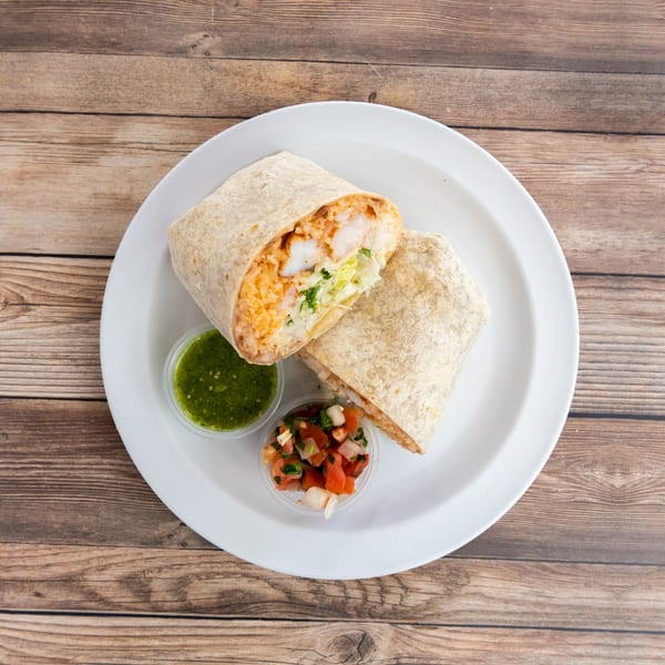 Two fish burritos, one cut in half, with green salsa and pico de gallo on a white plate.
