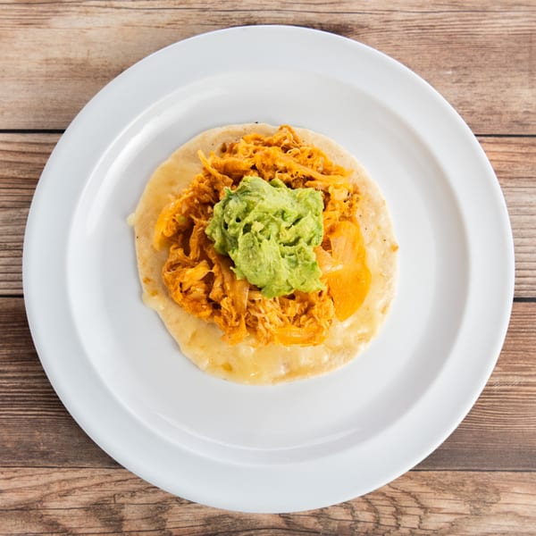 A single chicken taco with guacamole on a white plate, on a wooden table.