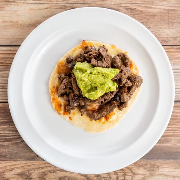 Overhead view of a single taco with steak, melted cheese, and guacamole on a white plate.