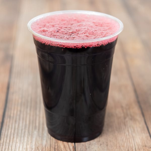 Dark red juice with a foamy top in a clear plastic cup on a wooden surface.