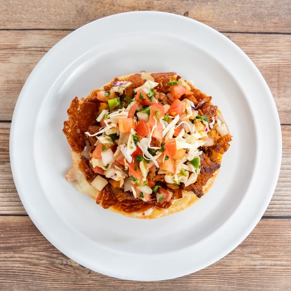 A crispy tostada topped with seasoned meat, shredded cabbage, diced tomatoes, and onions on a white plate.