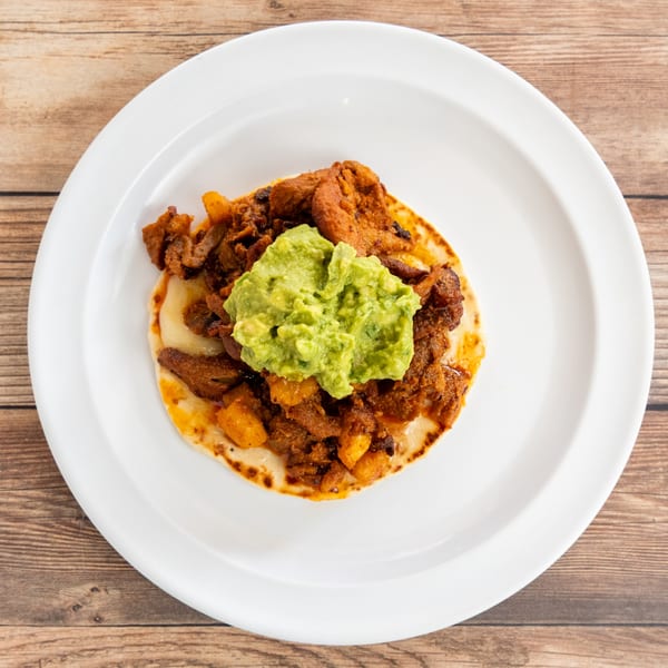 A single taco with red meat, pineapple, and guacamole on a white plate.
