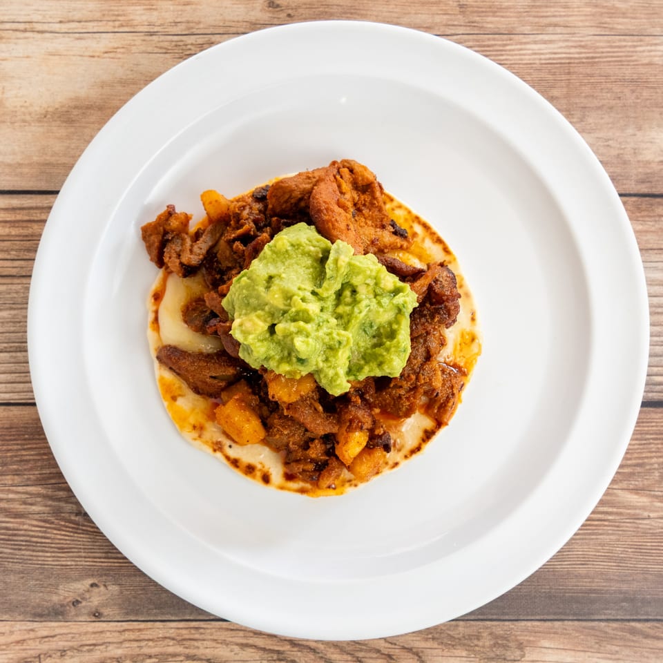 A single taco with red meat, pineapple, and guacamole on a white plate.