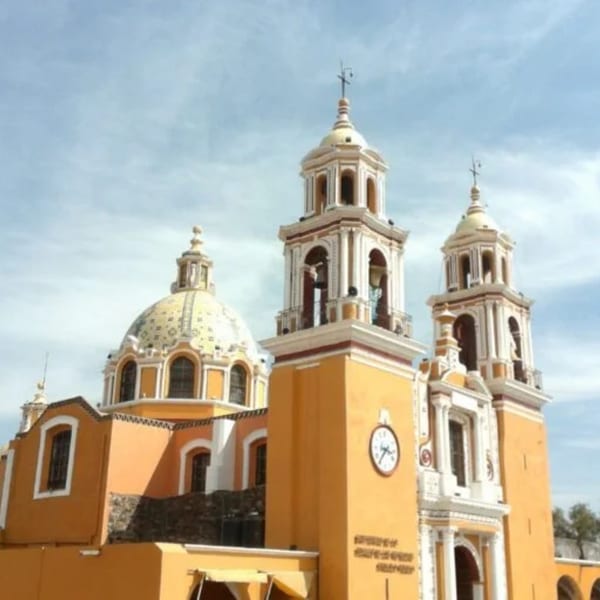 The vibrant yellow and white Cholula pyramid church with a dome and bell towers under a blue sky.