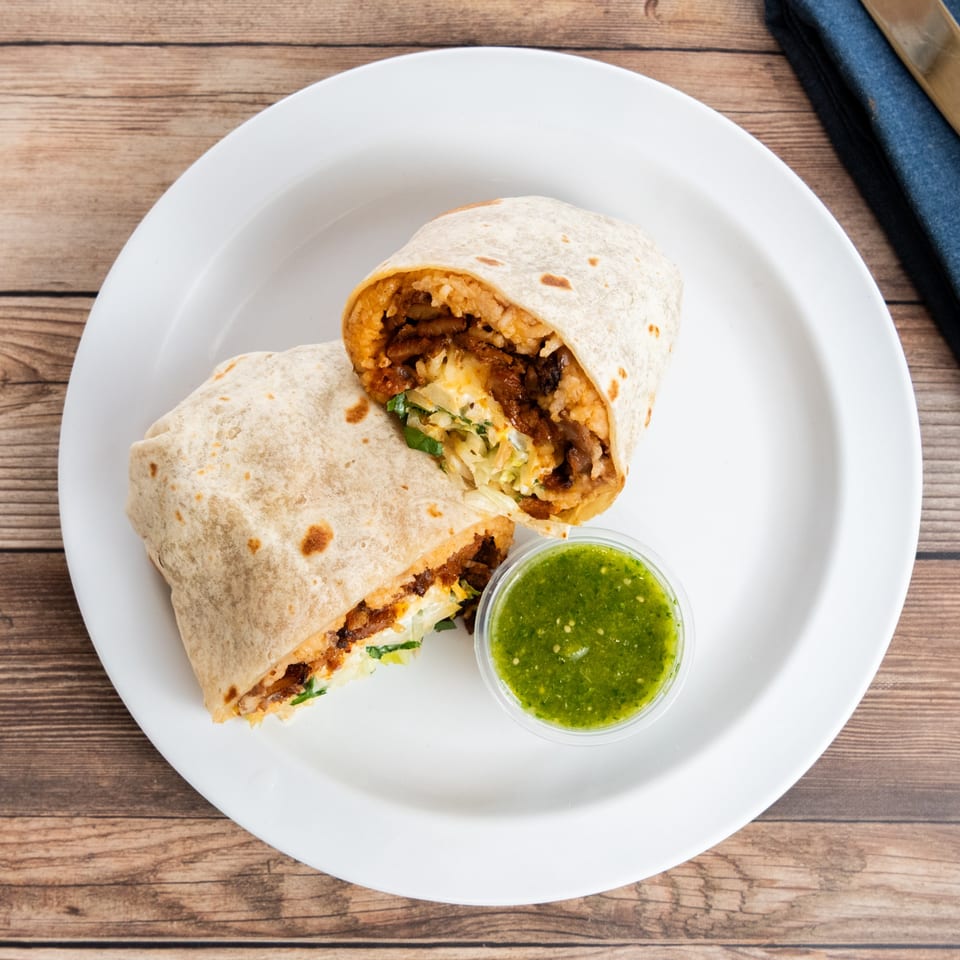 Two halves of a burrito filled with meat, rice, and vegetables, served with green salsa.